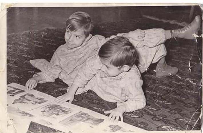 Dve deti v pyžamách ležia na koberci a prezerajú si časopis. Retro čiernobiela fotografia.
