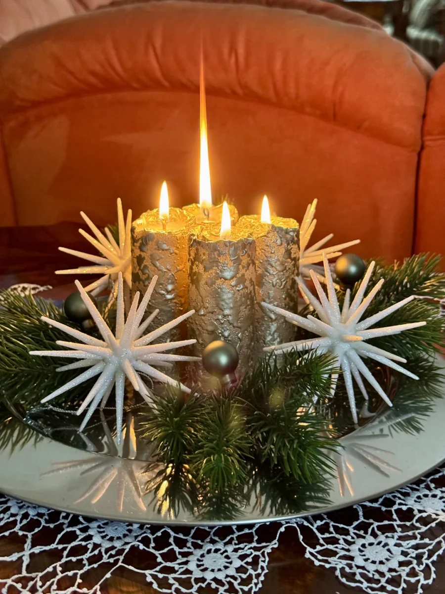 Adventný veniec so štyrmi horiace sviečky, bielymi hviezdami a zelenými vetvami na zrkadlovom podnose.