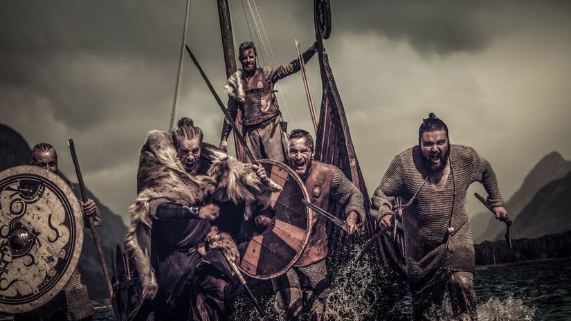 Skupina Vikingov vystupuje z lode na pobreží, pripravená na dobrodružstvo v dramatickom, historickom prostredí.