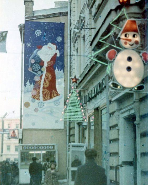 Zimná ulica s vianočnou výzdobou, veľkým obrazom Mrazíka a svetelným snehuliakom.