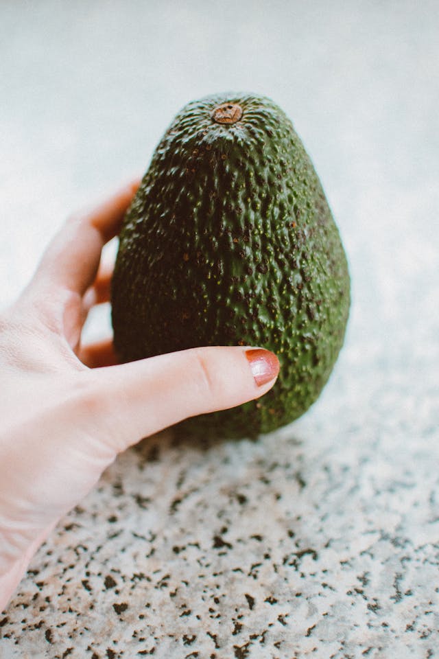 Ruka drží zrelé avokádo na kamennej doske, ideálne na guacamole.