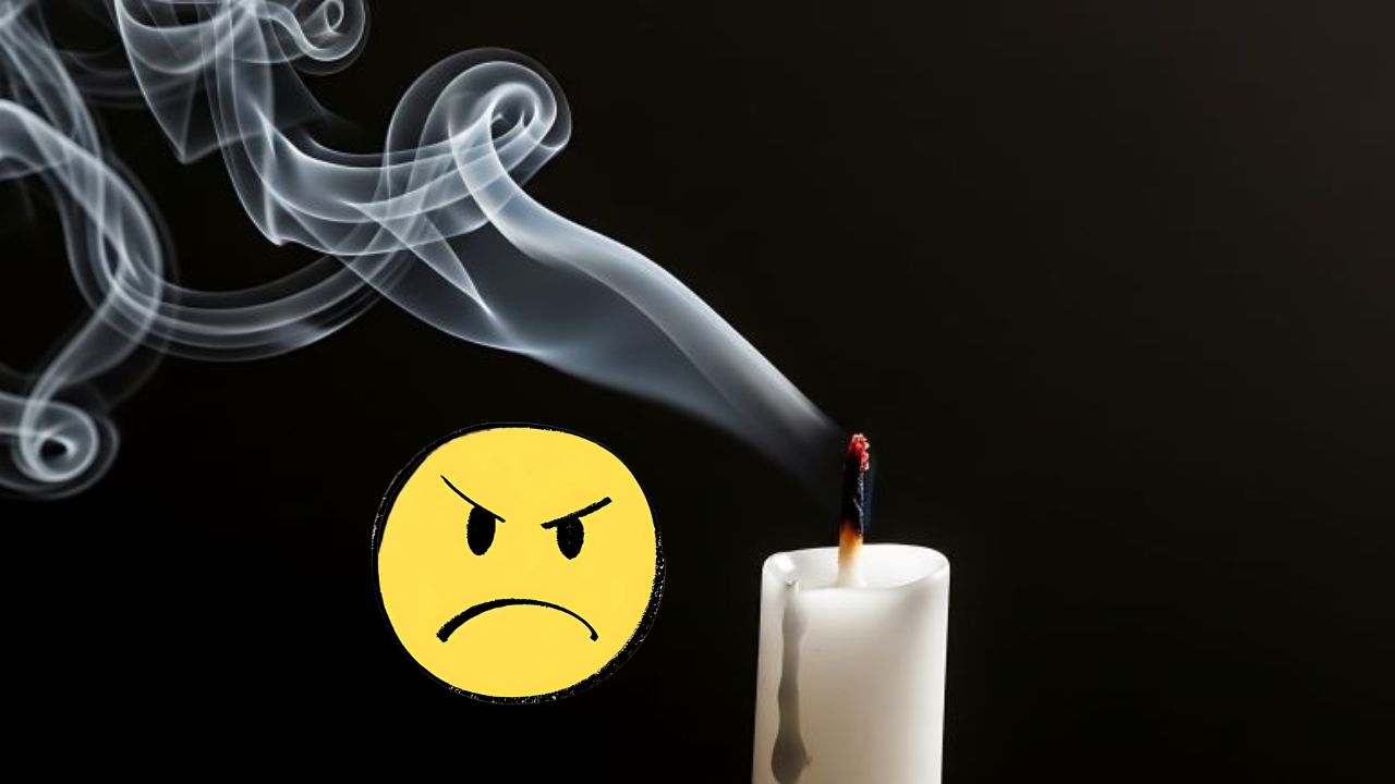Zhasnutá sviečka s dymom a nahnevaný emotikon na tmavom pozadí.