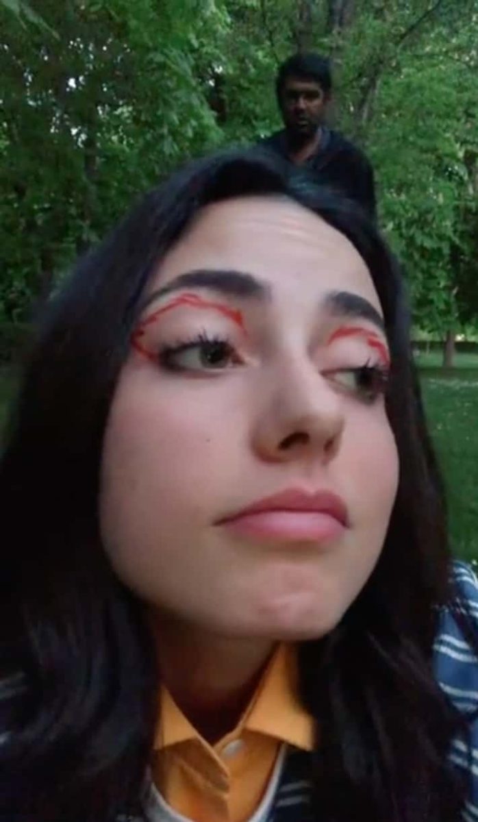 Osoba s kvetinovým líčením očí v lese za súmraku, zahľadene do diaľky.