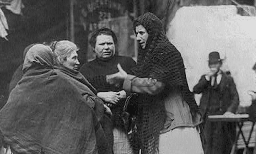 Skupina žien v tradičnom oblečení rozprávajúca sa na ulici, vintage čiernobiela fotografia.