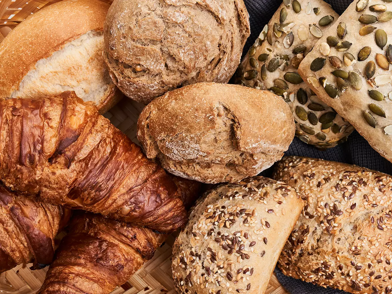Rôzne druhy čerstvého pečiva vrátane croissantov a semienkových rohlíkov v košíku.