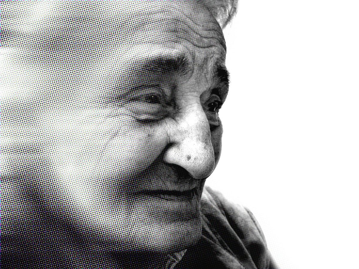Staršia žena s výrazom múdrosti a pokoja v čiernobielej bodkovanej úprave.