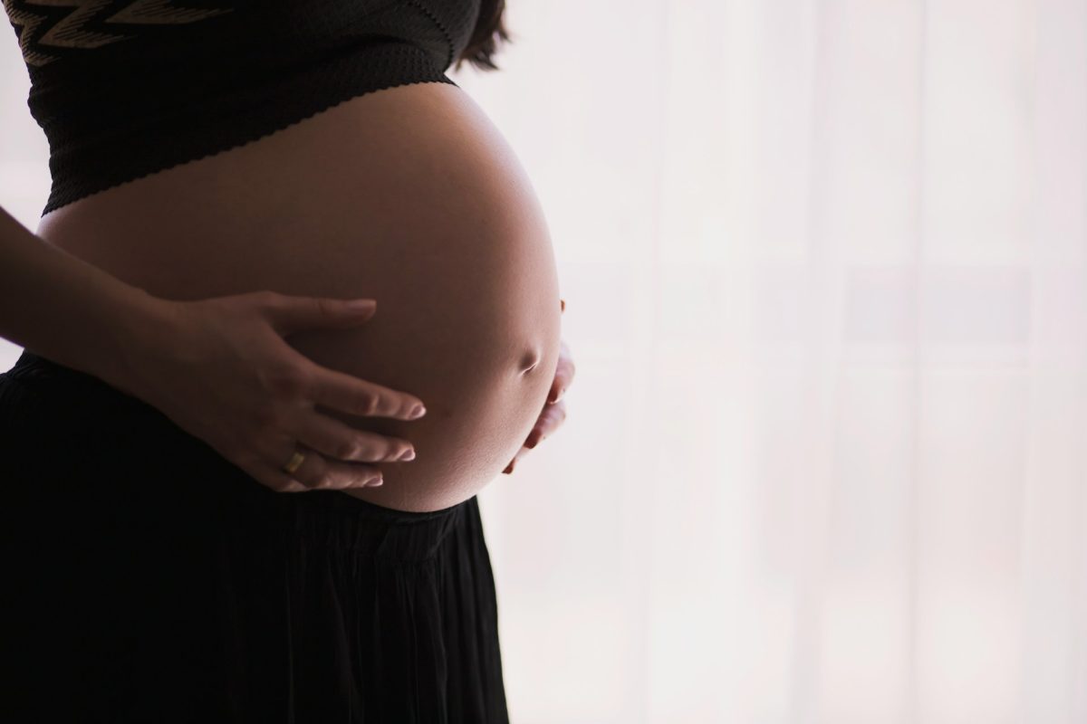 Tehotná žena si jemne drží brucho, zachytená v pokojnom prostredí. Vnímanie materstva a nového života.