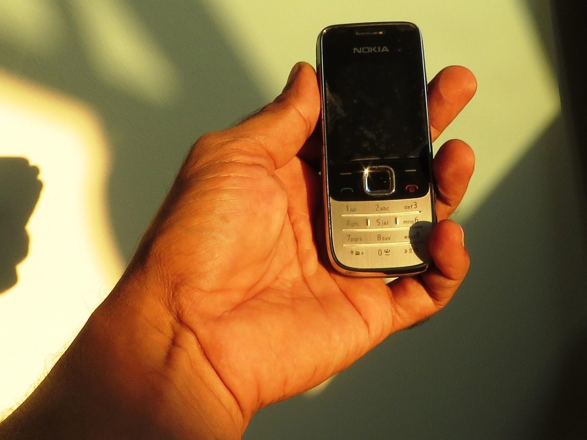 Ruka drží starší tlačidlový telefón Nokia so slnkom osvetlenou klávesnicou, detail retro technológie.