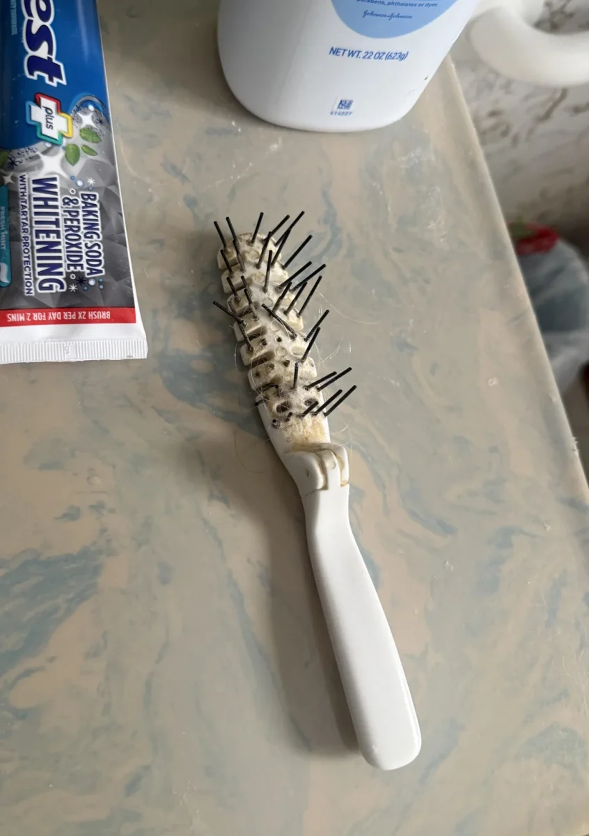 Zubná kefka s poškodenými štetinami položená na kúpeľňovej doske vedľa pasty a pleťovej vody.
