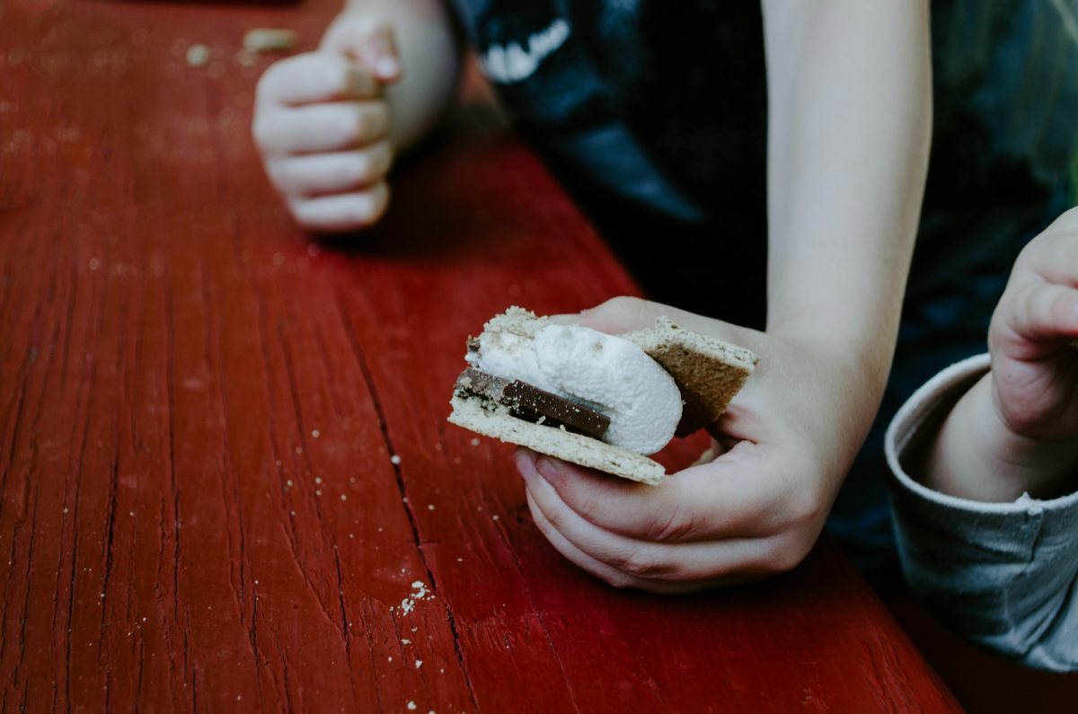 Dieťa drží sladký s'more s čokoládou a marshmallow nad červeným stolom.