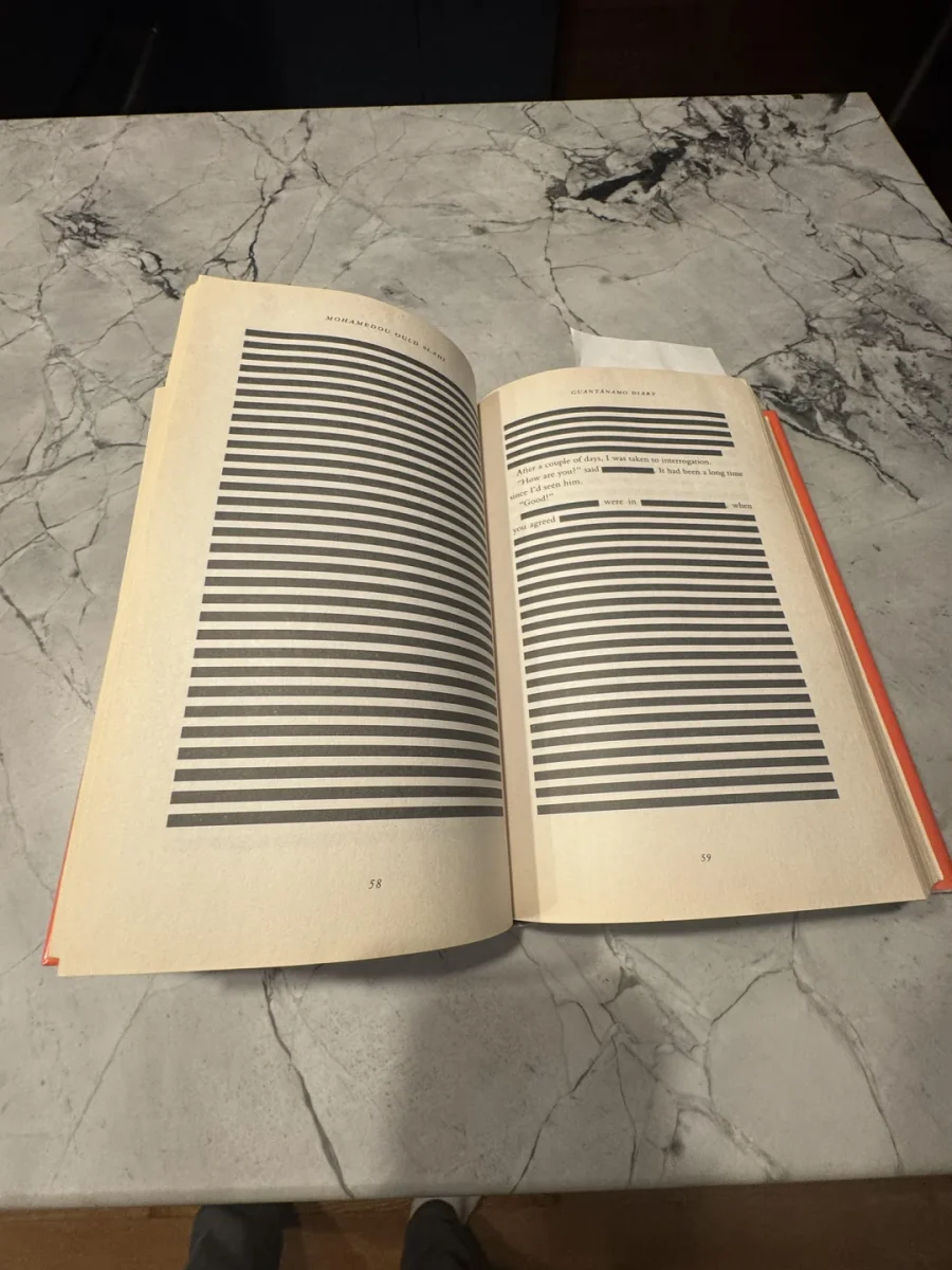 Kniha s cenzurovaným textom na otvorenej dvojstrane, položená na kamennom stole.
