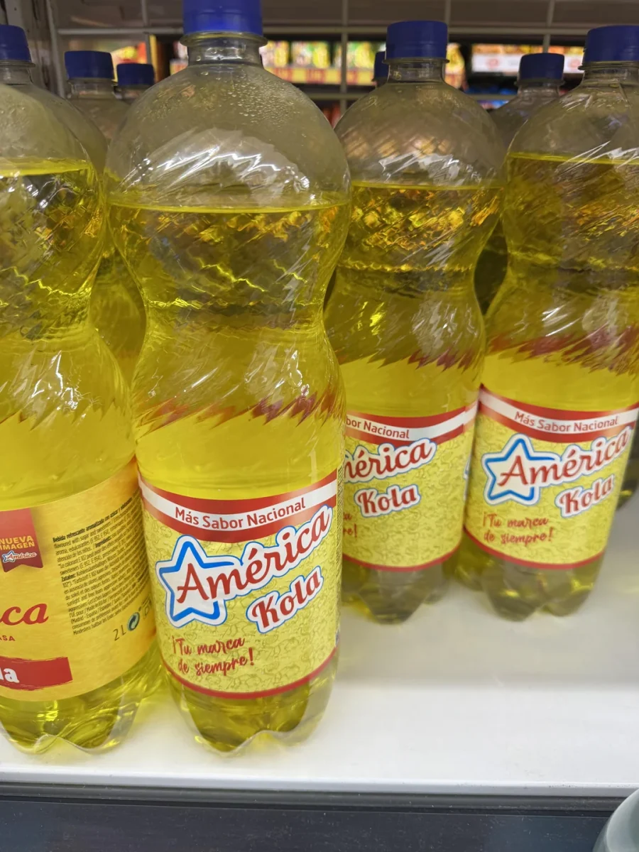 Fľaše America Kola so žltou etiketou vystavené na regáli v obchode.