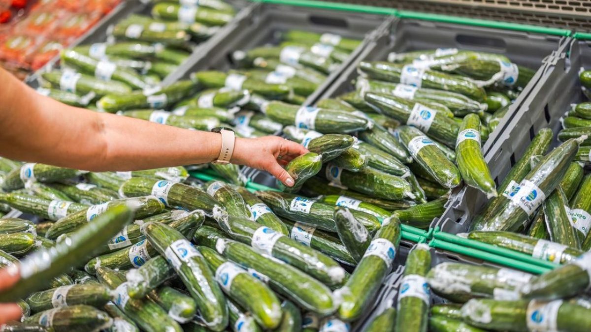 Ruka vyberá zabalenú uhorku z regálu v supermarkete.