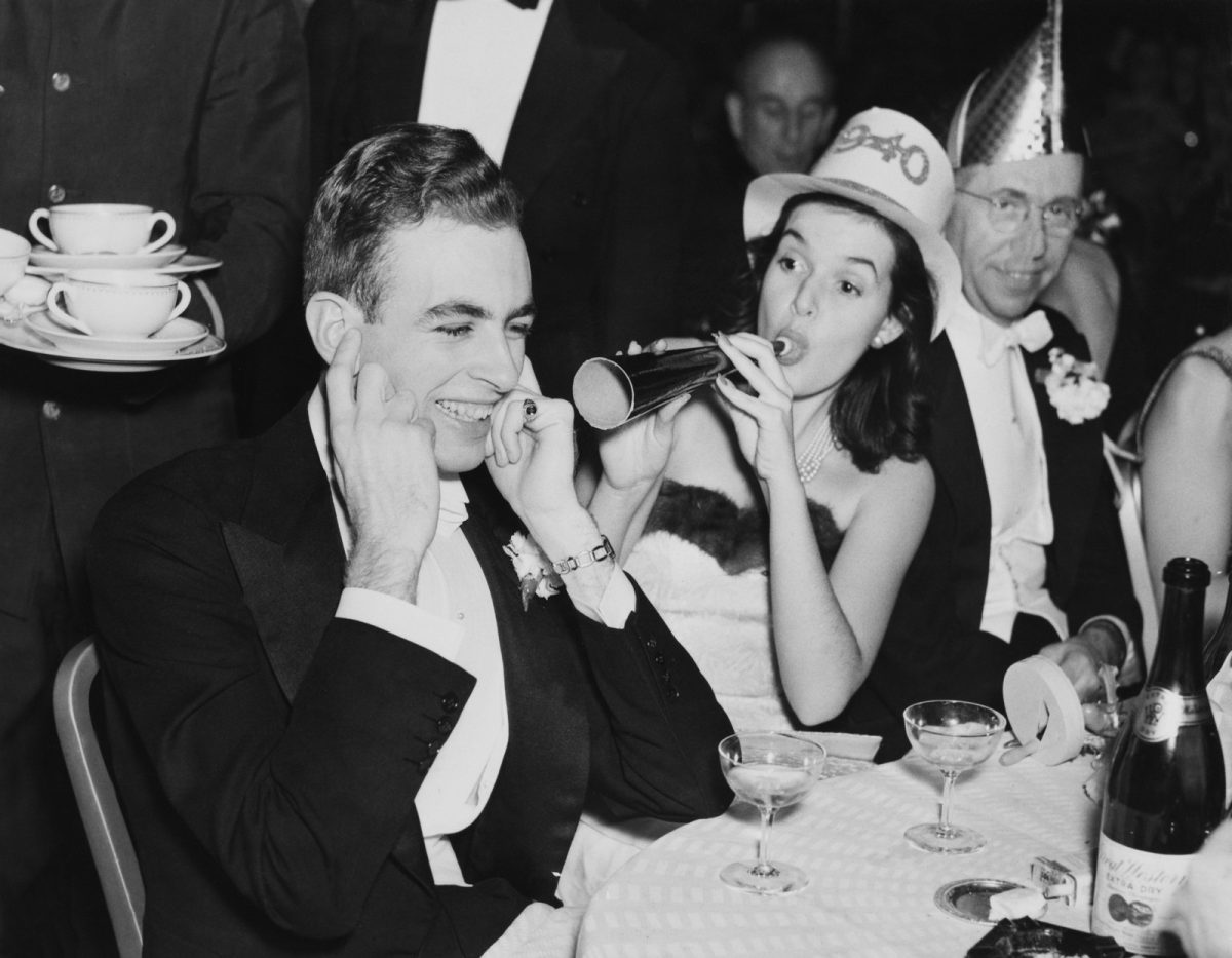 Oslava Nového roka v 40. rokoch, muži v smokingu a žena s trumpetu, bavia sa v elegantnom prostredí.