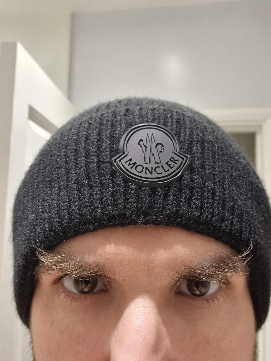 Čierna pletená čiapka s logom Moncler na hlave nositeľa, zobrazená zblízka.