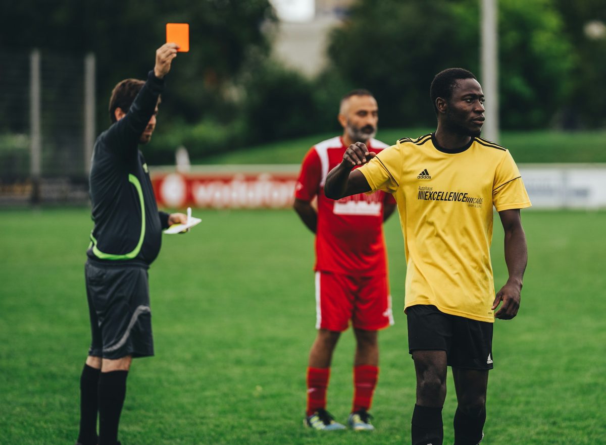 Rozhodca ukazuje červenú kartu futbalistovi v žltom drese na futbalovom ihrisku.