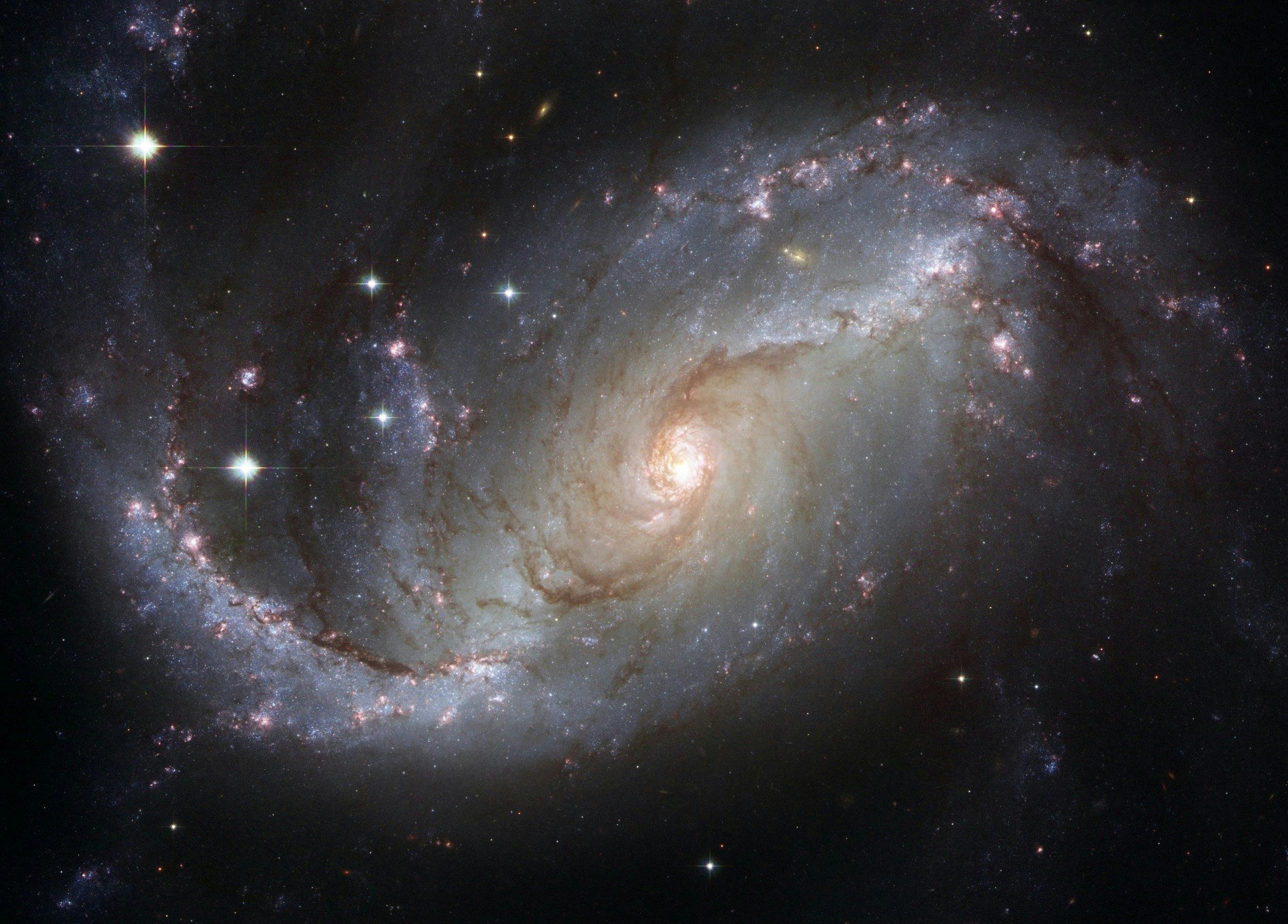 Špirálová galaxia s jasnými hviezdami a hmlovinami v tmavom vesmíre, zachytená teleskopom Hubble.