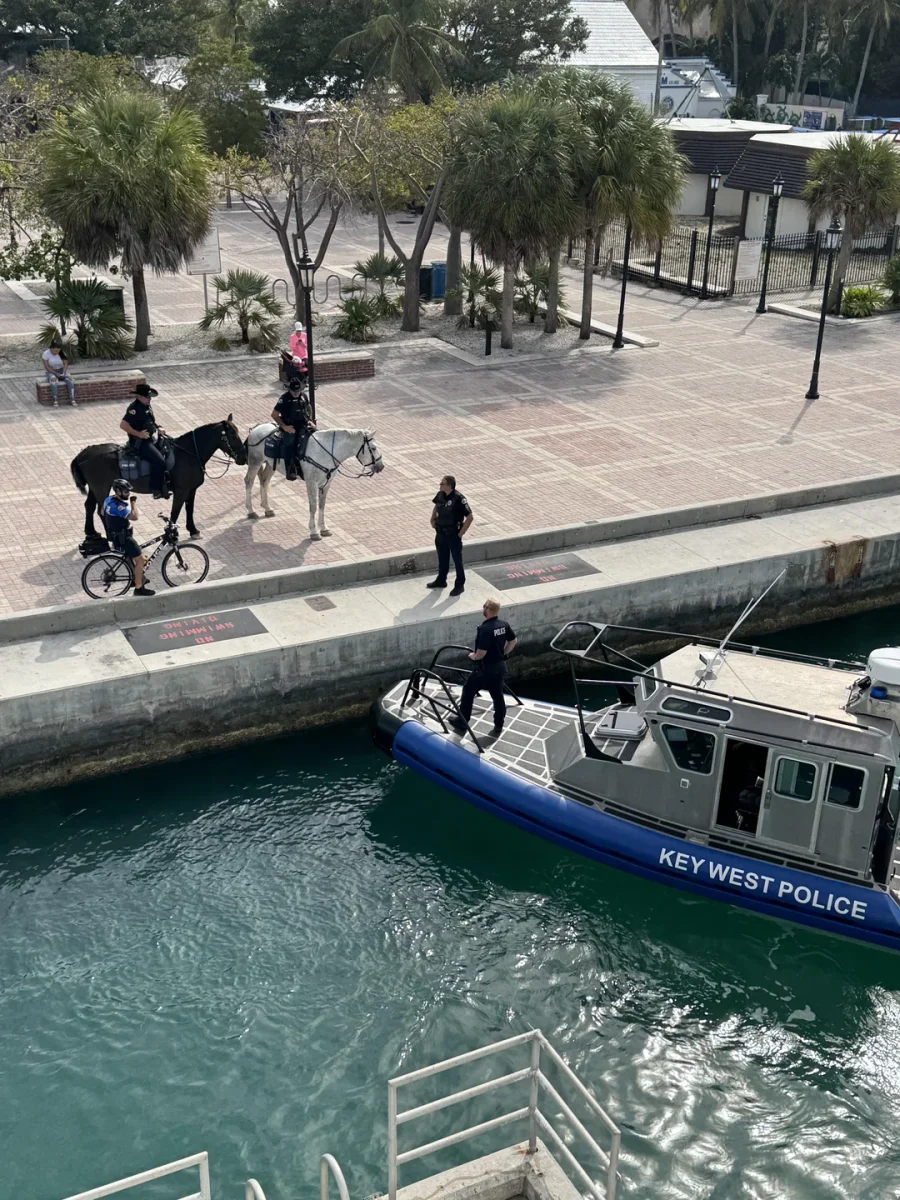 Policajti na bicykli, koňoch a člne na Key West v blízkosti pláže a palmy.