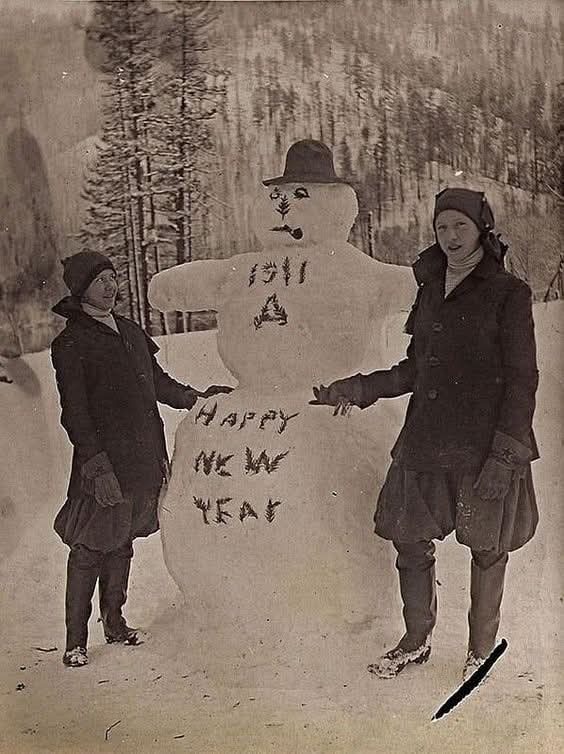Dve ženy pri snehuliakovi s textom 1911 Happy New Year v zasneženej krajine. Retro zimná pohoda.