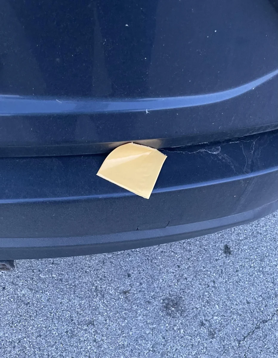 Žltý štvorcový papierový štítok medzi dvomi časťami tmavého automobilu na parkovisku.