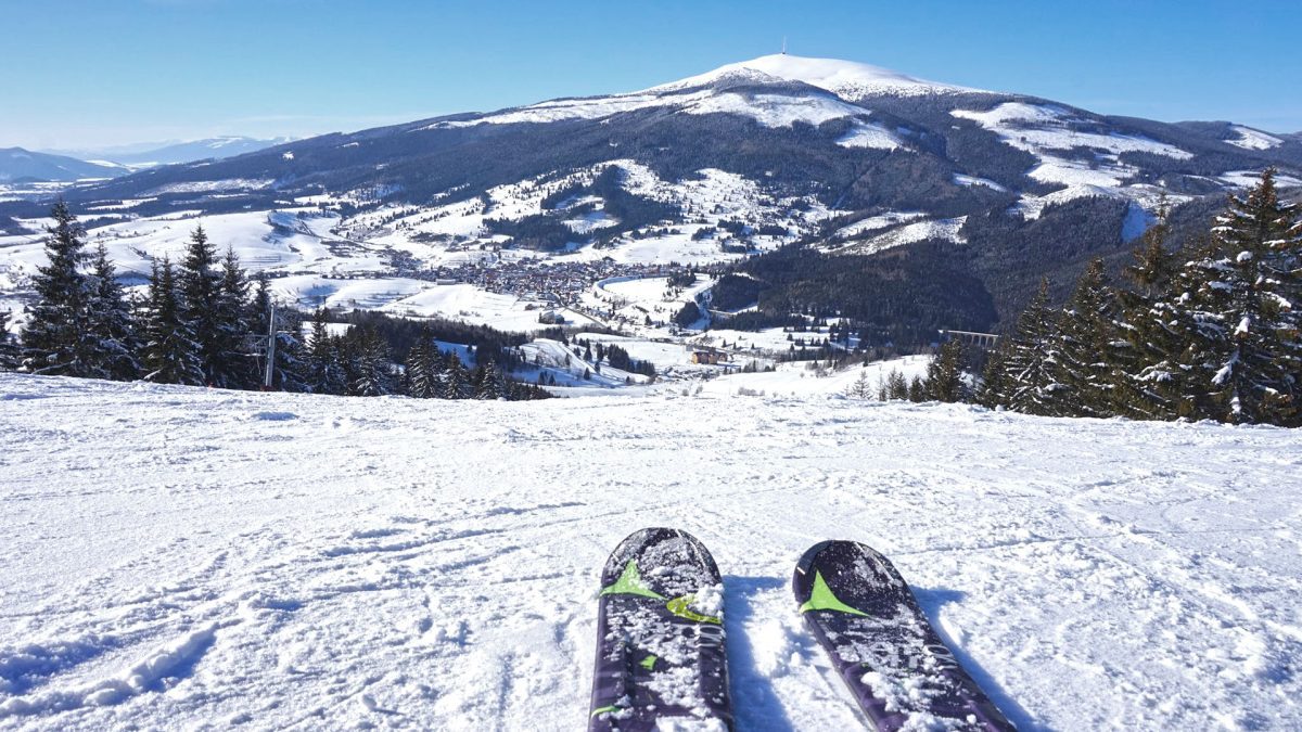 Lyžiarska stopa na vrchole slovenského kopca s panoramatickým výhľadom na zasneženú krajinu a modrú oblohu.