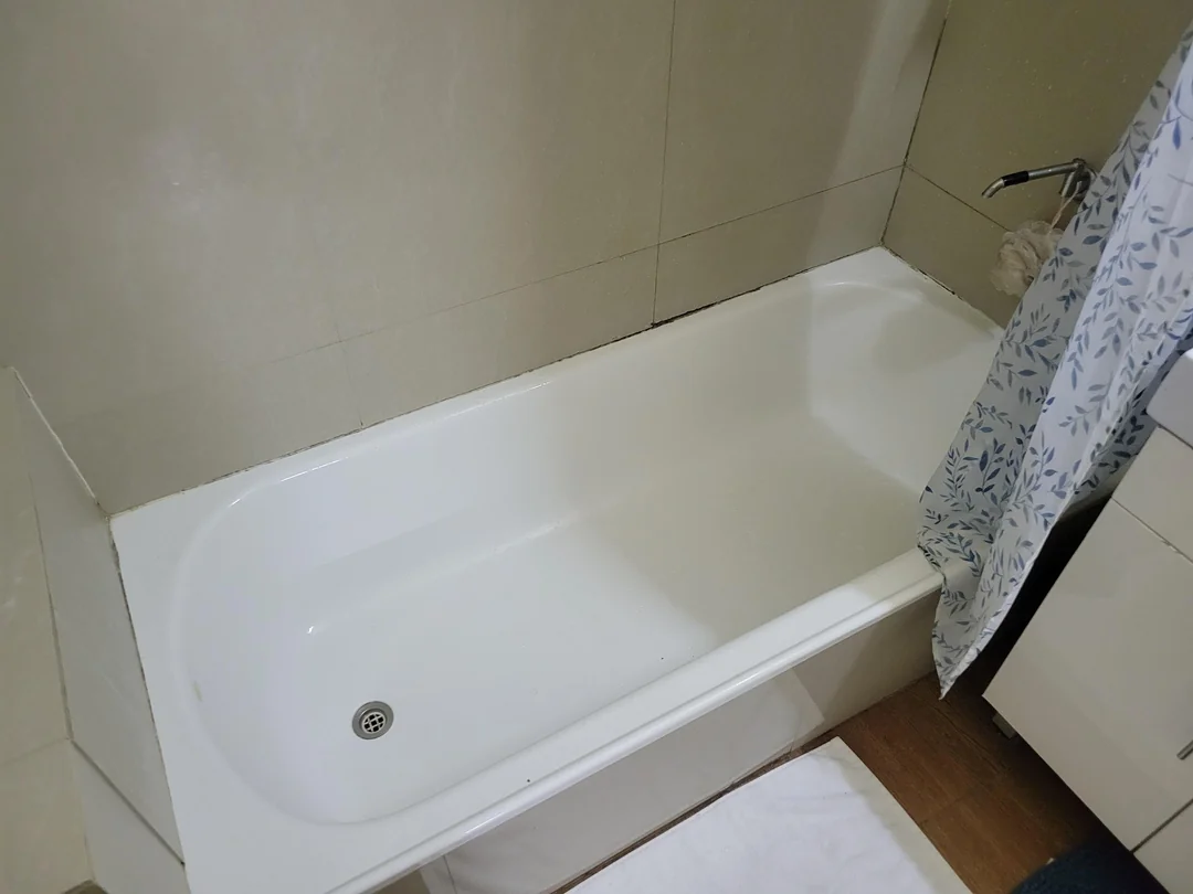 Biela vaňa v moderne zariadenej kúpeľni s dekoratívnym závesom a drevenou podlahou.