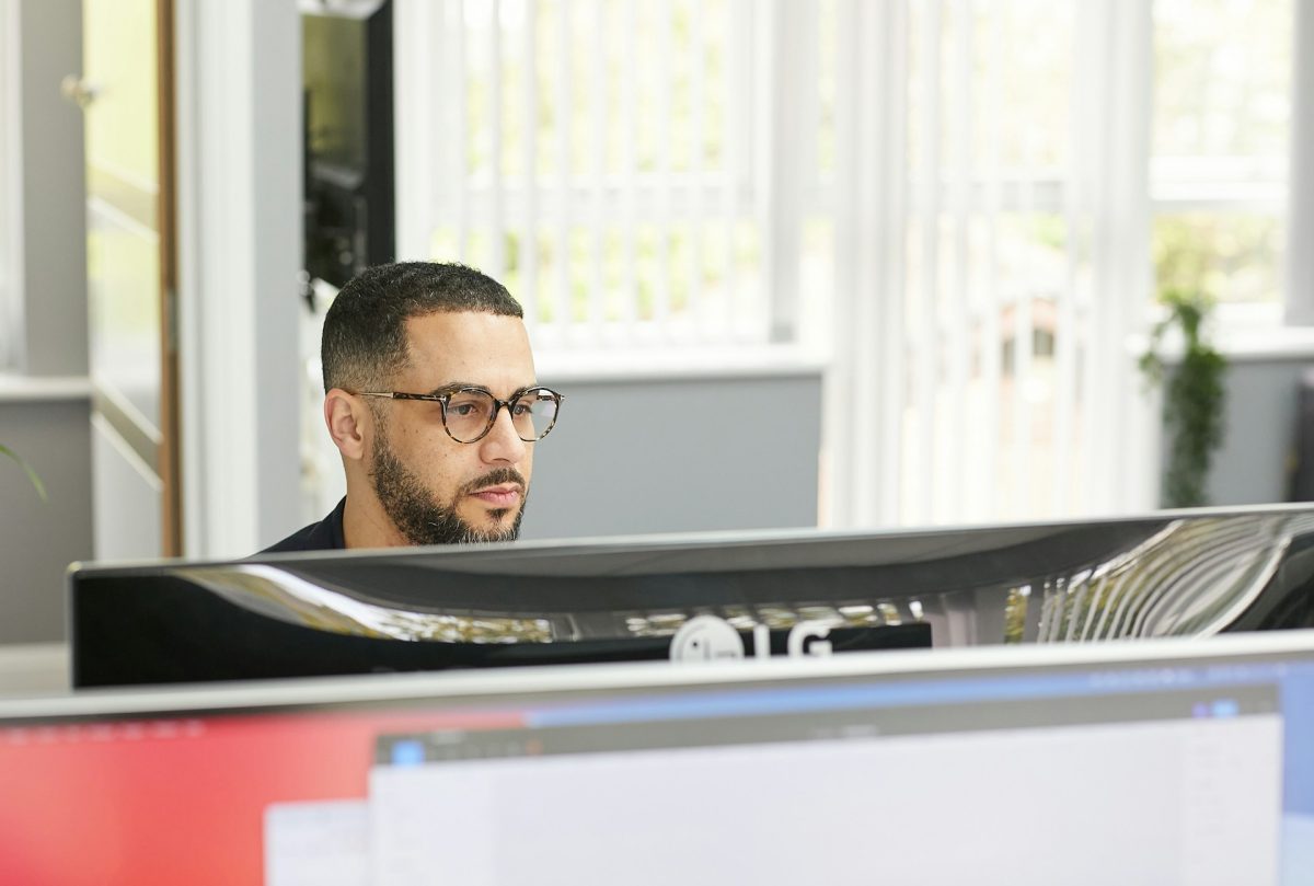 Muž pracujúci na počítači v kancelárii, sústredený na monitor s oknom v pozadí.