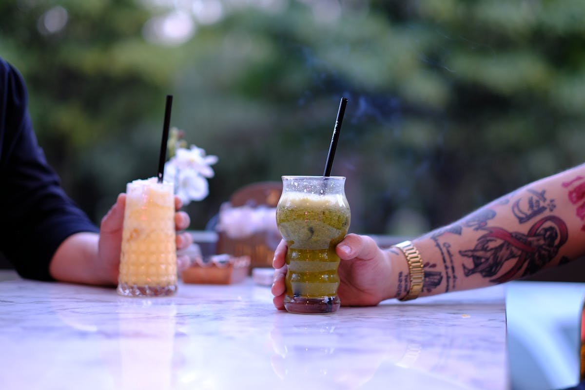 Two people enjoy colorful bubble tea drinks with straws in an outdoor setting.