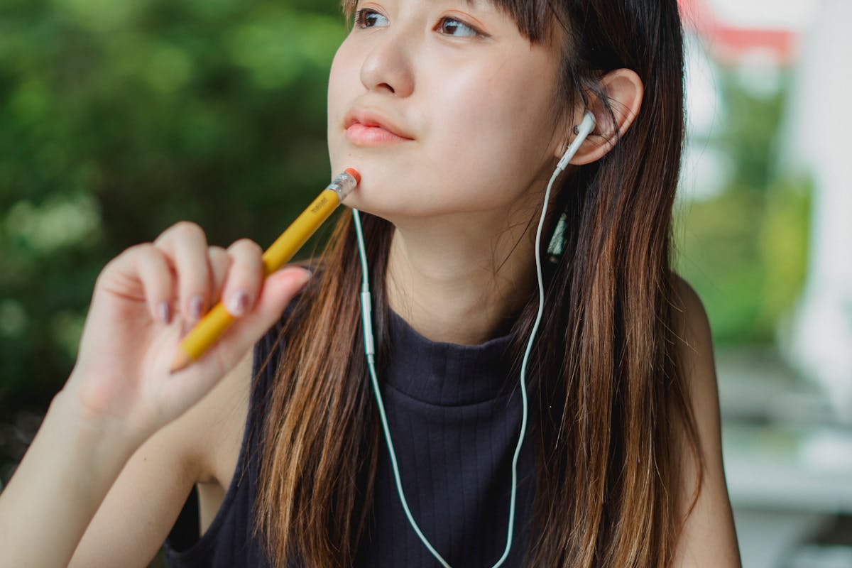 A young woman listens to music with earbuds while contemplating outdoors.
