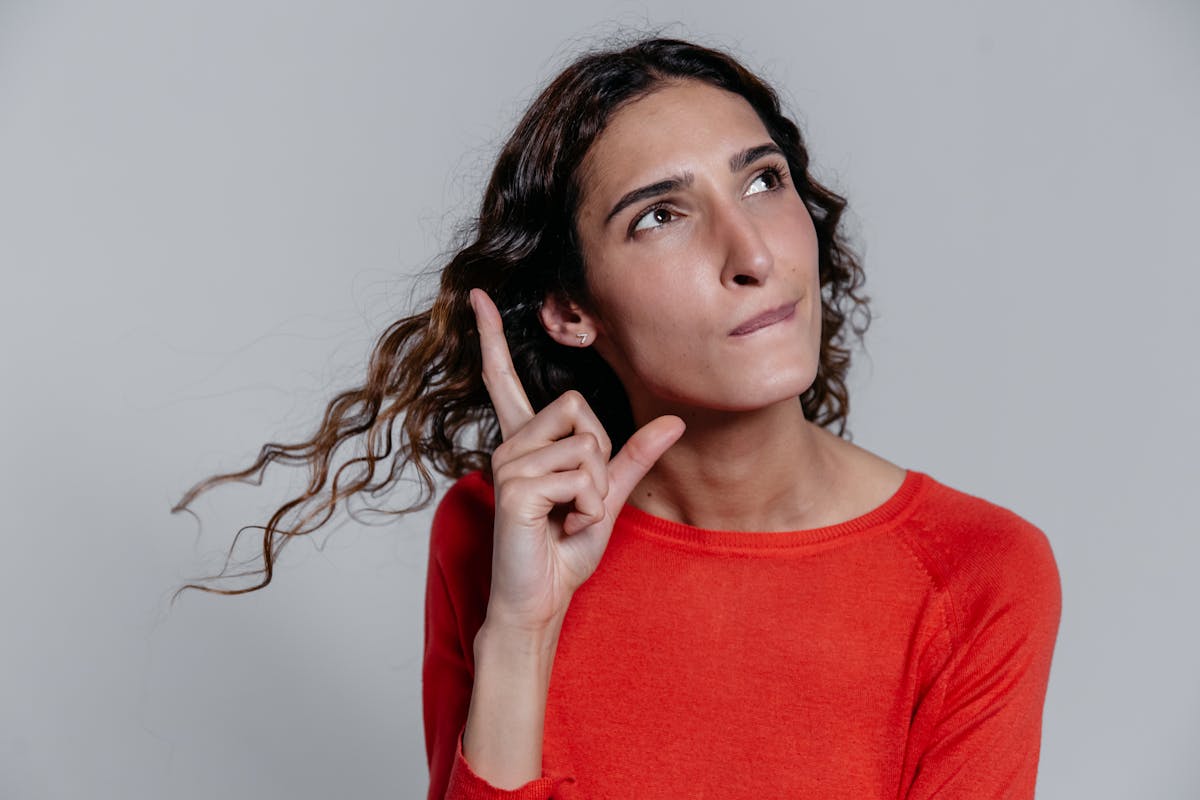 Contemplative woman pointing upwards, thinking deeply in a casual setting.