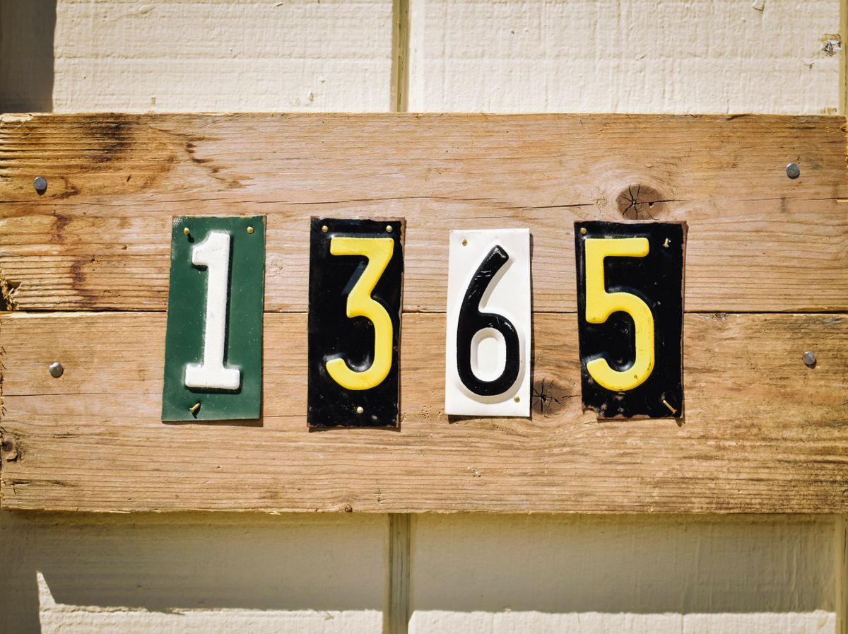 Rustic wooden house number sign with colorful digits 1365 on weathered planks, outdoors.