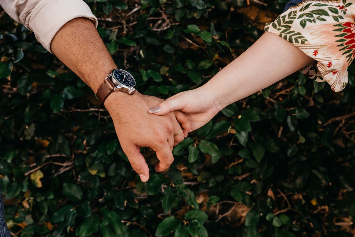A close-up of a couple holding hands against a leafy background, symbolizing connection.