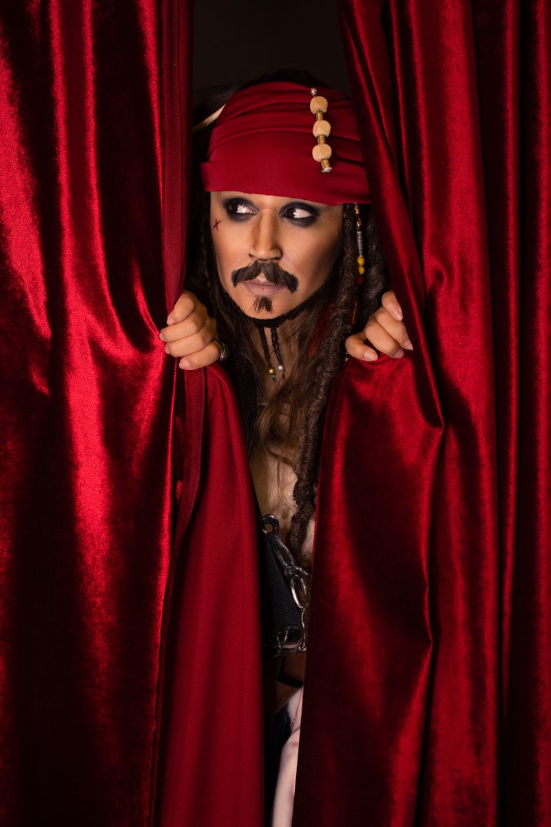 A person dressed as a pirate peeks through vibrant red curtains.