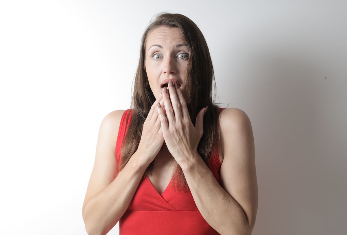 A surprised young woman in a red dress reacting dramatically against a plain white background.