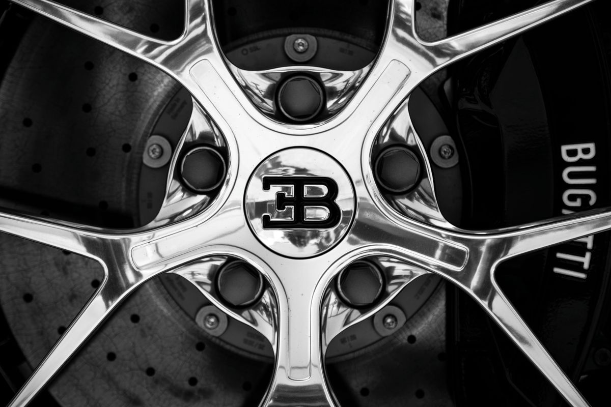 Black and white close-up shot of a Bugatti car rim showing intricate design and luxury branding.