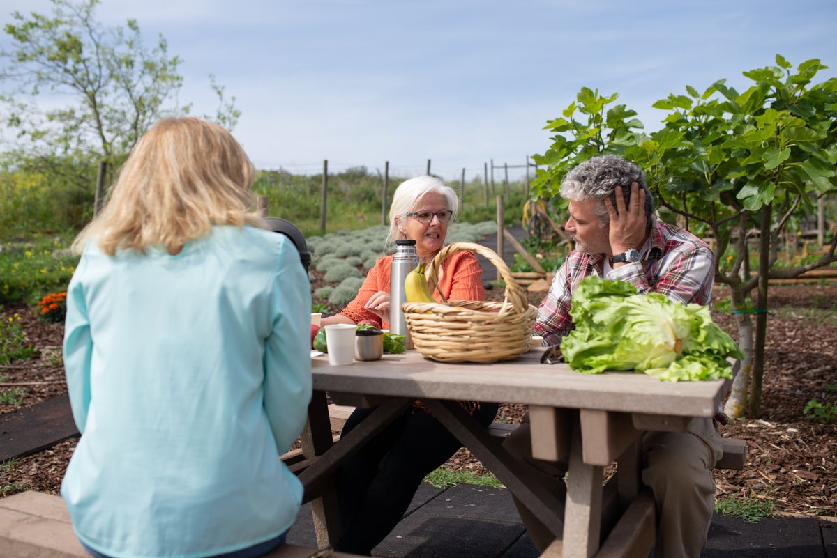 Senior adults at a picnic table enjoying a meal in a vibrant garden setting.